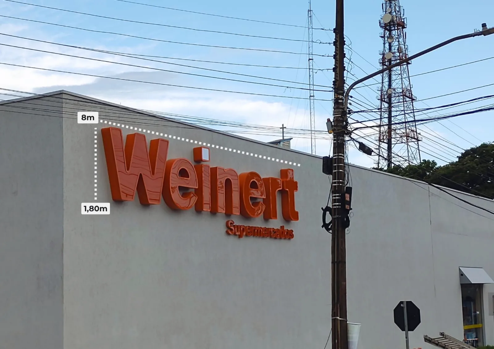 Letreiro em letra caixa laranja da Weinert Supermercados instalado na parede do mercado, com medidas de 8 metros por 1,80 metro