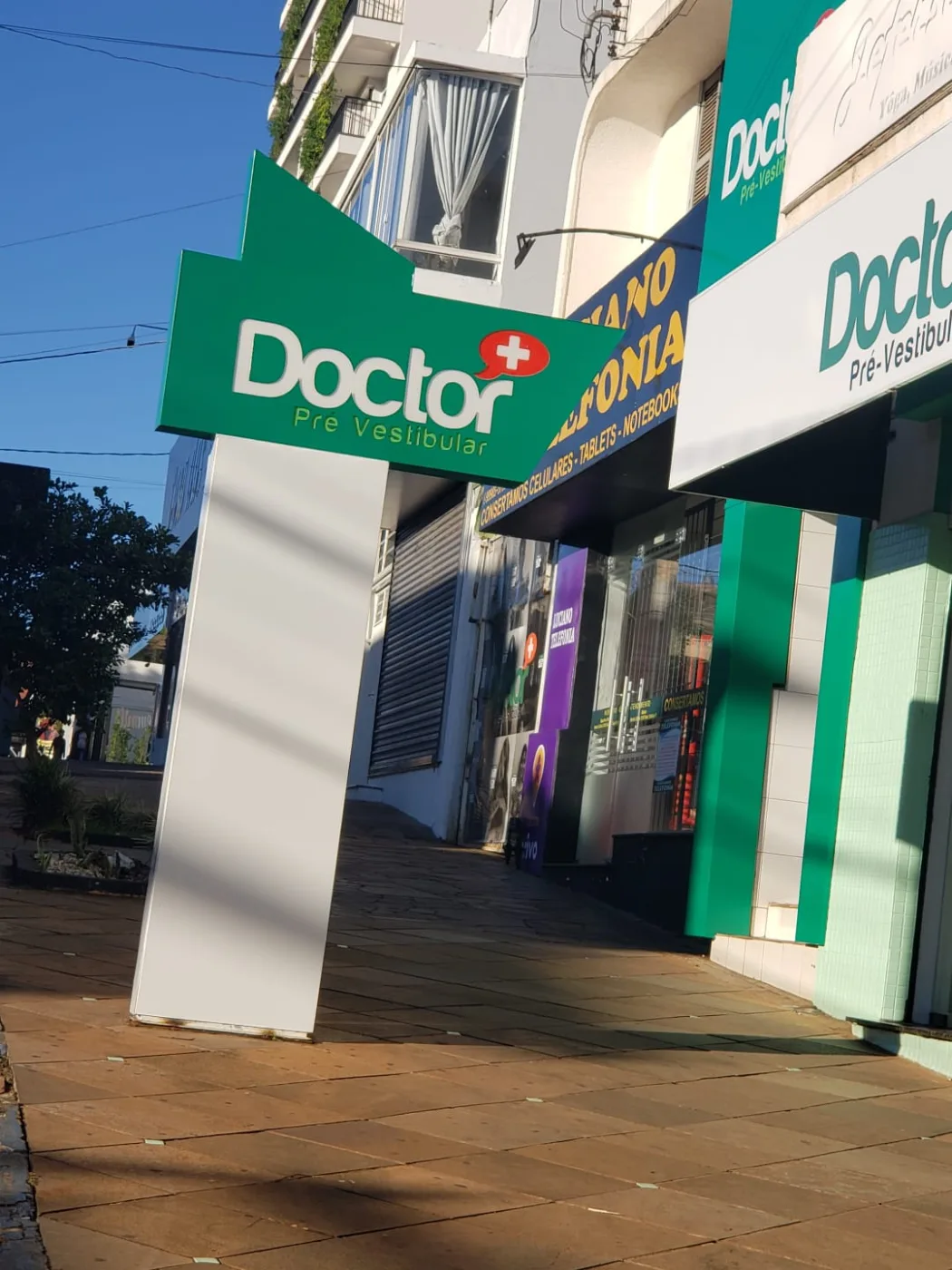 Totem branco com placa verde recortada da Doctor Pré-Vestibular na calçada