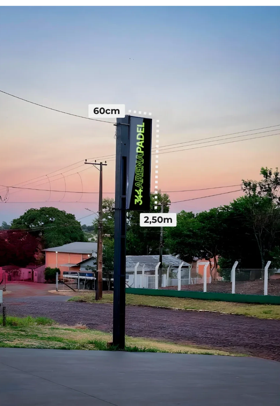 Totem vertical preto com letras verdes da Arena Padel, com 60 centímetros por 2,50 metros, ao pôr do sol